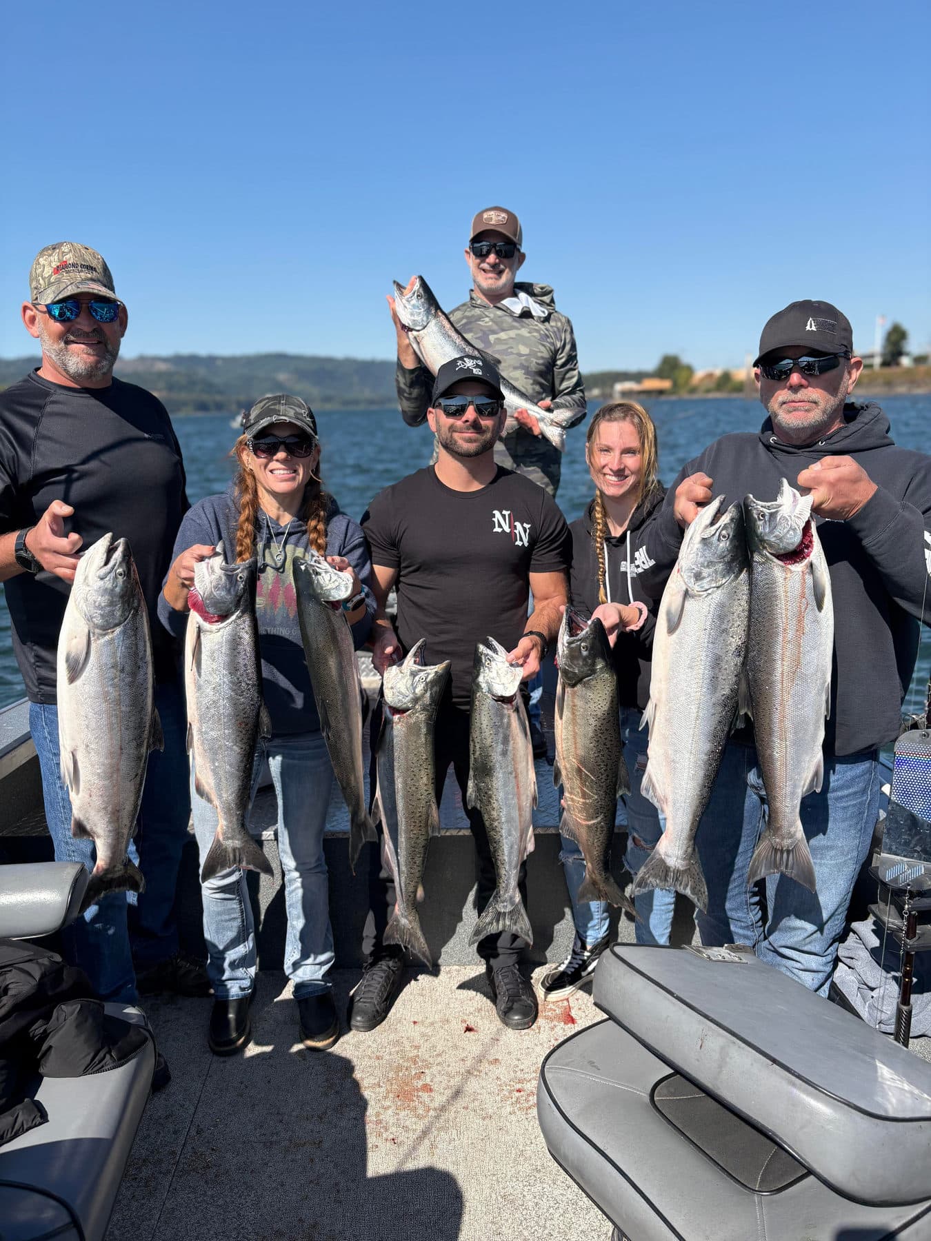 Six smiling anglers holding their salmon on the boat with the Columbia River behind them